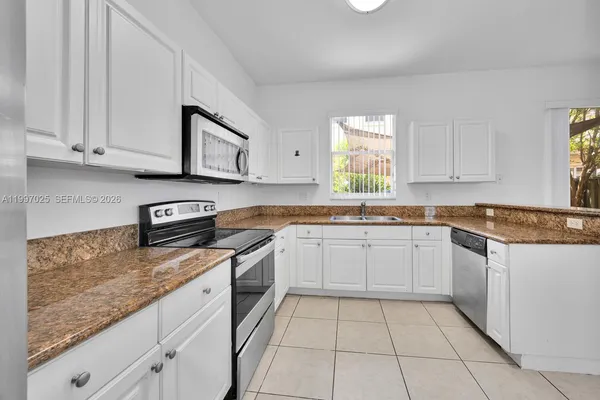 a kitchen with granite countertop white cabinets stainless steel appliances a sink and a window