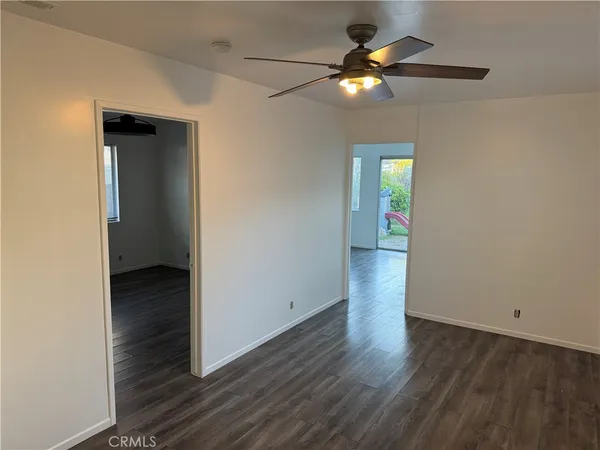 a view of an empty room with wooden floor and a fan