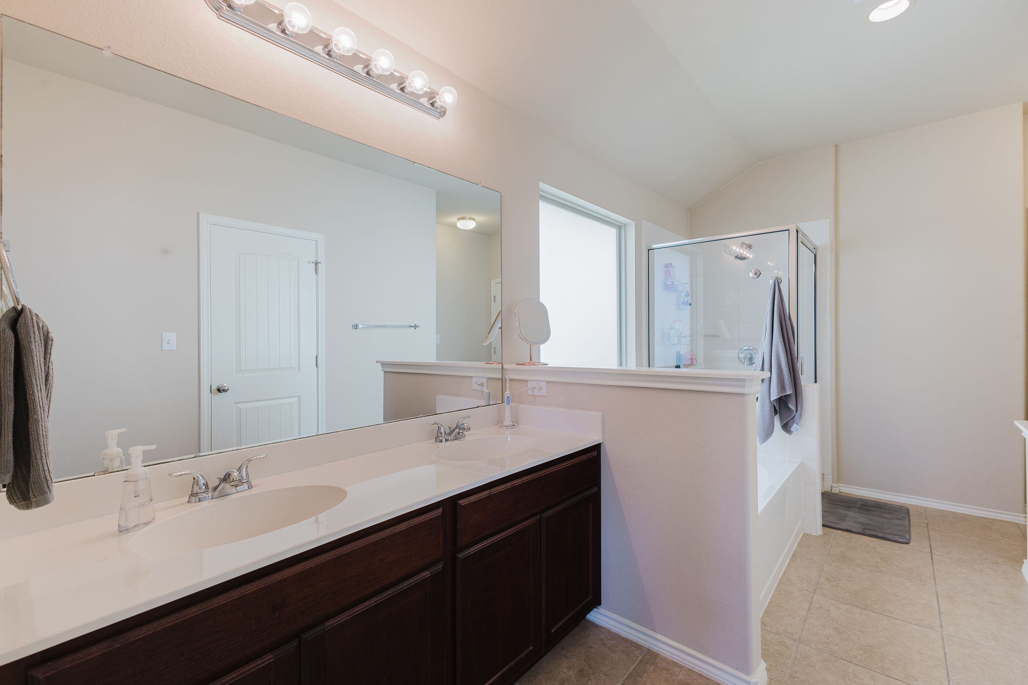 2292 Intrepid Drive Buda, TX 78610 - Photo 10 of 38 Full bathroom featuring double vanity, a shower stall, light tile patterned floors, vaulted ceiling, and a bath