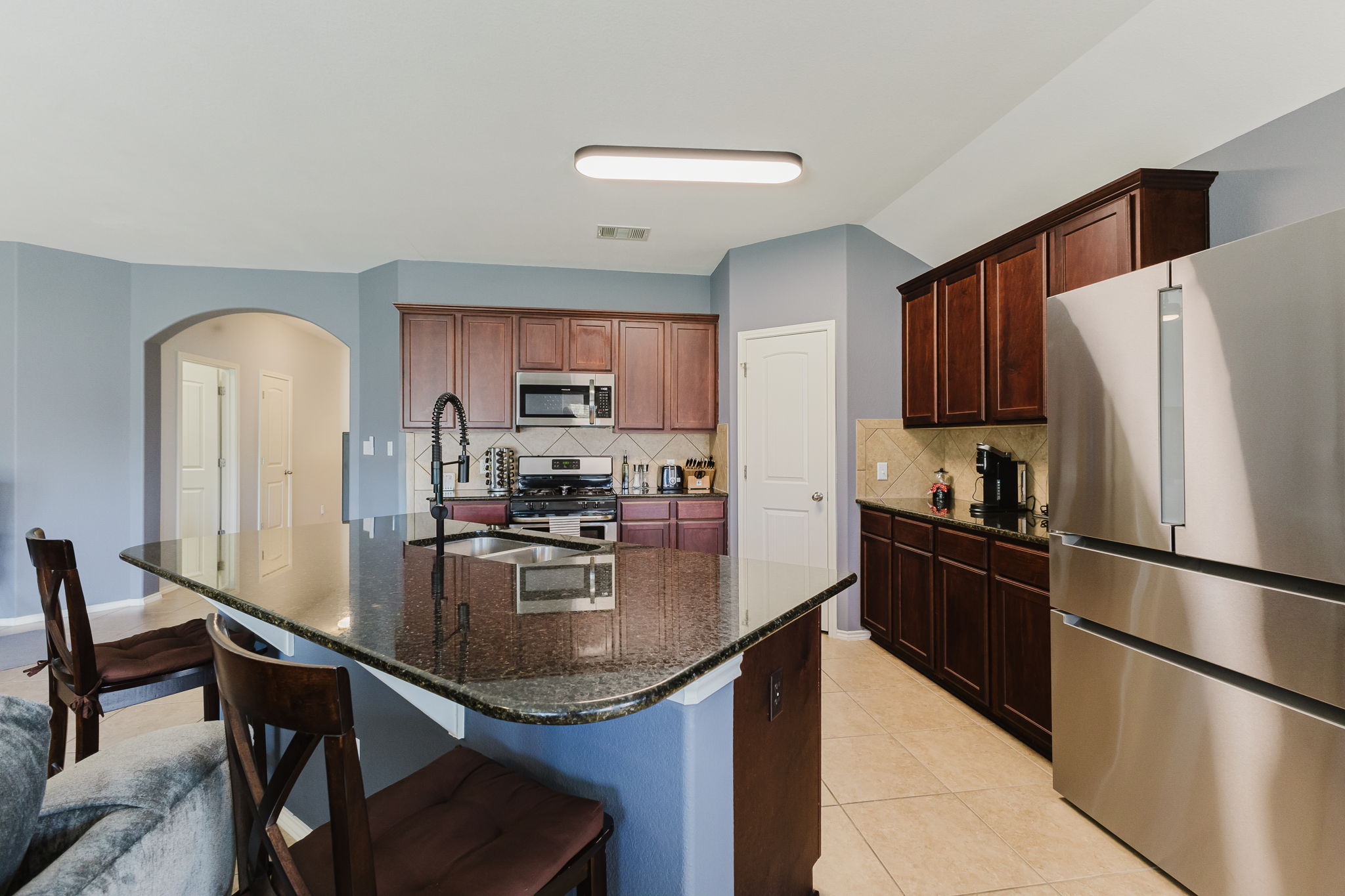 2292 Intrepid Drive Buda, TX 78610 - Photo 5 of 38 Kitchen with stainless steel appliances, arched walkways, dark stone countertops, a kitchen breakfast bar, and light tile patterned floors