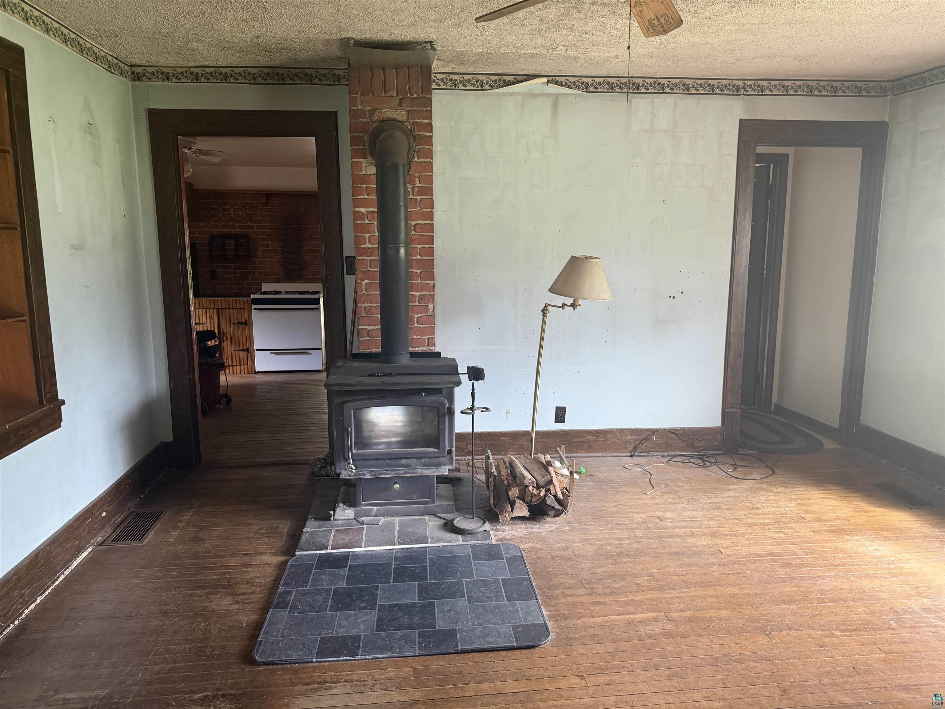 3541 Bent Trout Lake Road Barnum, MN 55707 - Photo 13 of 41 Room featuring wood-finish flooring, a brick-clad wood-burning stove with a stovepipe, and dark wood trim around doorways and a window
