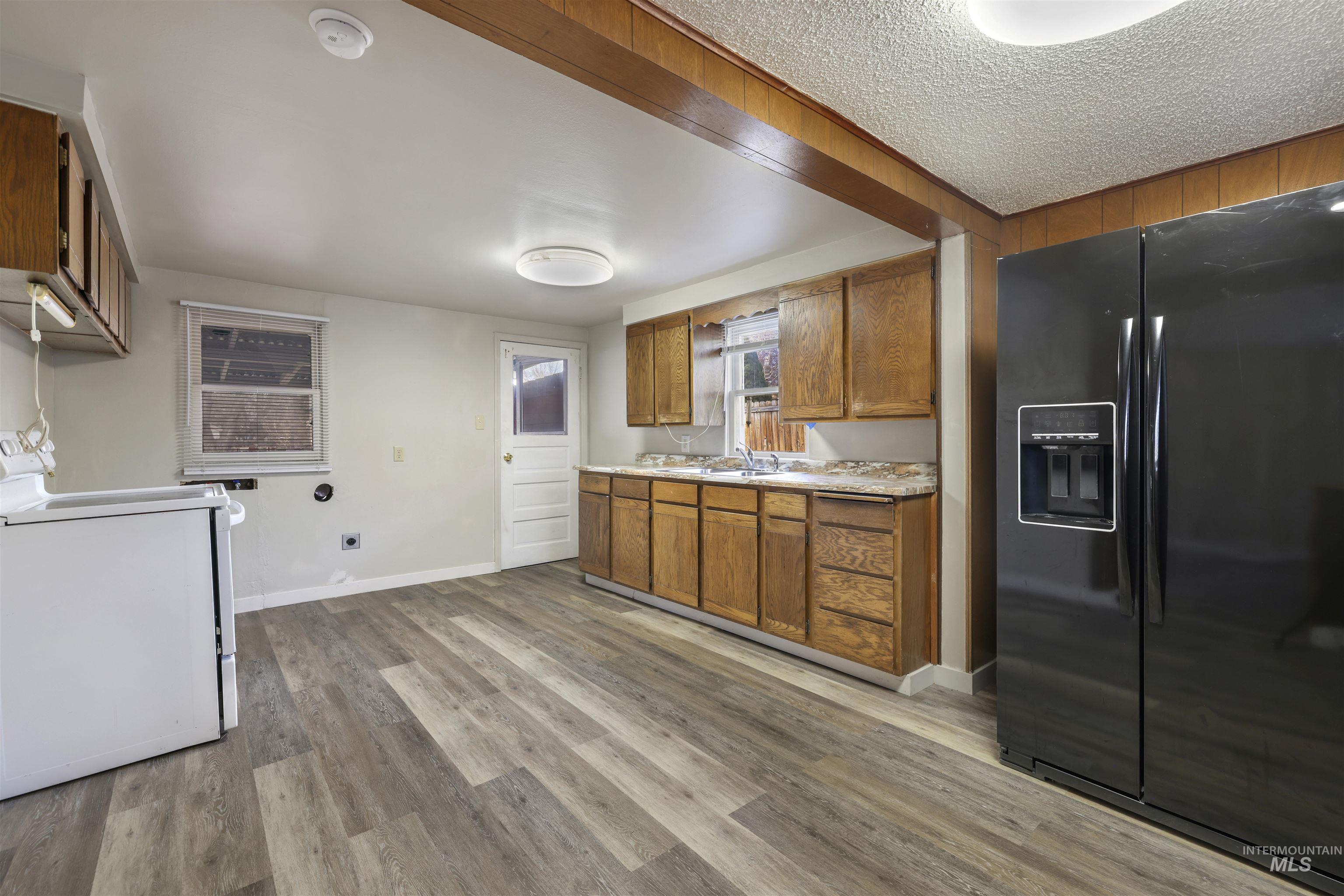 545 Madison Street Twin Falls, ID 83301 - Photo 4 of 23 Kitchen with black refrigerator with ice dispenser, brown cabinetry, light countertops, washer / clothes dryer, and light wood-type flooring