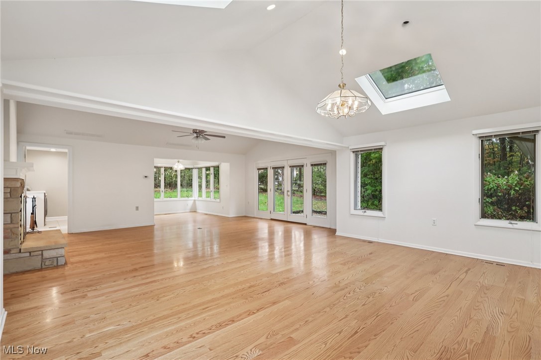 33300 South Woodland Road Cleveland, OH 44124 - Photo 19 of 50 Unfurnished living room featuring a skylight, light wood-style floors, a chandelier, a fireplace, and high vaulted ceiling