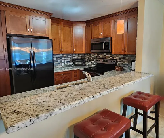 a kitchen with stainless steel appliances kitchen island granite countertop a refrigerator and a stove top oven