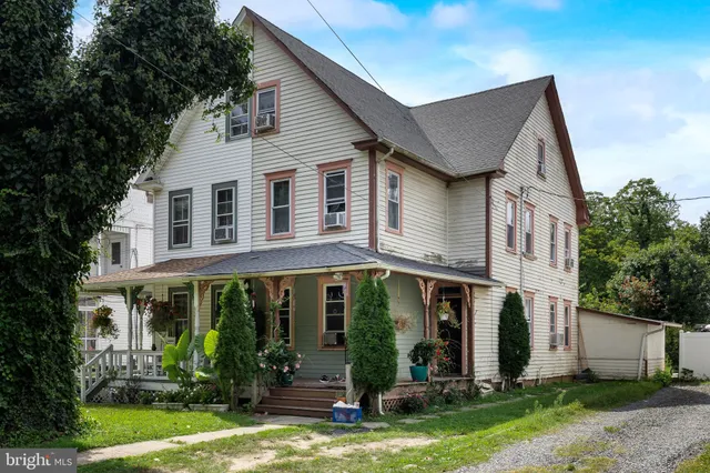a view of a white house with potted plants and a yard table and chairs
