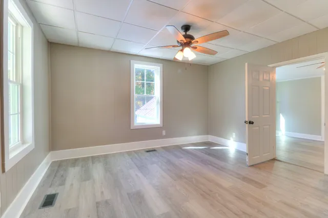an empty room with wooden floor chandelier fan and windows