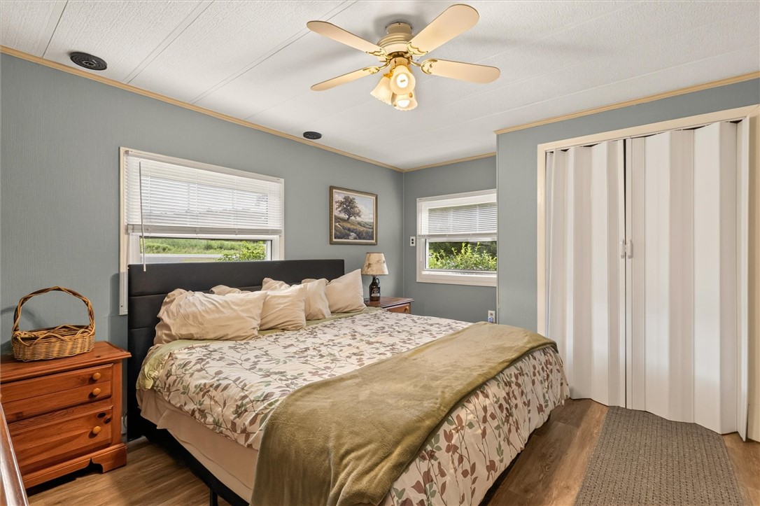 7213 Tilton Road Bristol, NY 14469 - Photo 20 of 50 Spacious primary bedroom with neutral blue-gray walls and warm wood flooring.
Multiple windows provide natural light and wooded/outdoor views.
Large double-door closet offers additional storage.
Ceiling fan adds comfort and airflow.