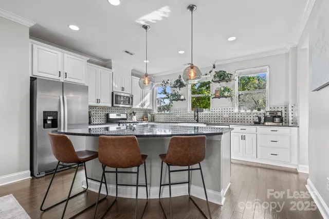 a kitchen with stainless steel appliances granite countertop a stove a refrigerator a sink a dining table and chairs with wooden floor