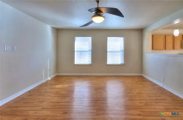 an empty room with wooden floor chandelier and windows
