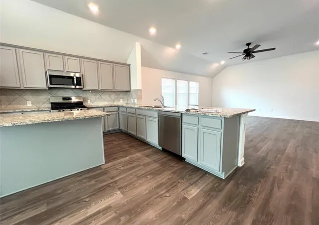a kitchen with stainless steel appliances granite countertop a sink a stove top oven and wooden floors