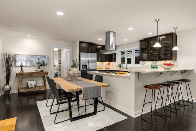 a kitchen with stainless steel appliances kitchen island granite countertop a refrigerator a stove a microwave oven a dining table and chairs with wooden floor