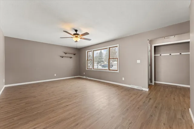 an empty room with wooden floor ceiling fan and windows