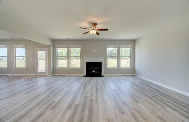 an empty room with wooden floor chandelier fan and windows