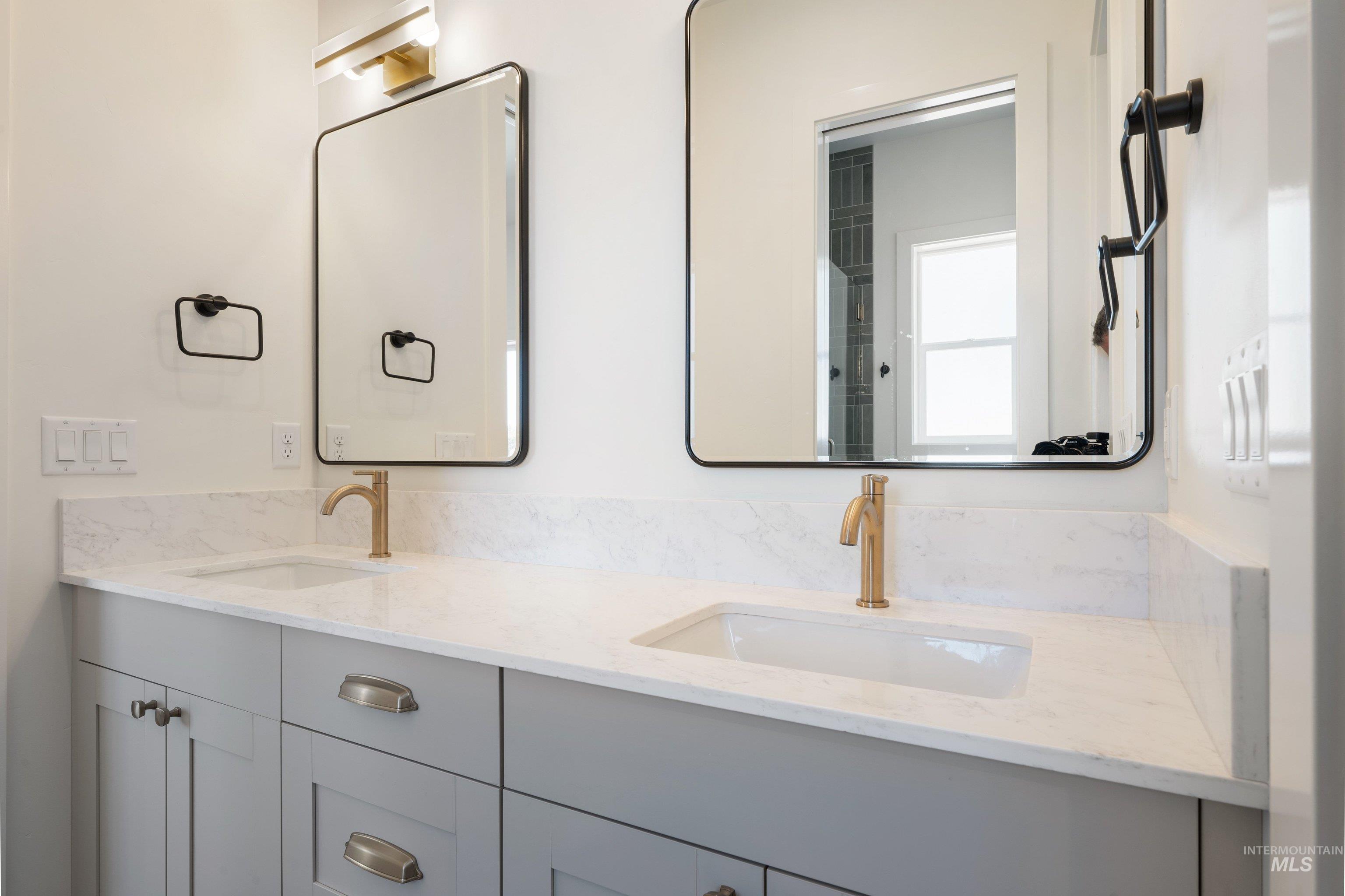 24821 Ardmore Court Caldwell, ID 83607 - Photo 32 of 43 Double vanity featuring light gray cabinetry, integrated sinks, brass-finish faucets, and white stone countertops