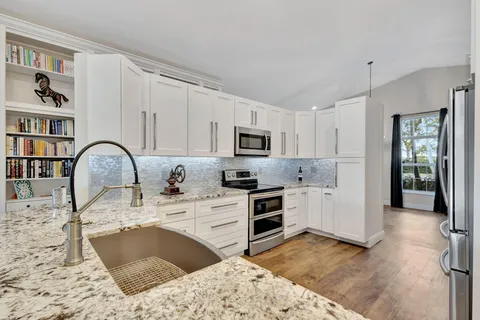 a kitchen with stainless steel appliances granite countertop a stove top oven a sink dishwasher and white cabinets with wooden floor