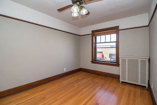 an empty room with wooden floor chandelier fan and windows