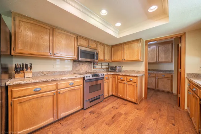 a kitchen with stainless steel appliances granite countertop a stove top oven a sink dishwasher and a refrigerator with wooden cabinets