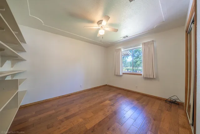 an empty room with wooden floor fan and windows