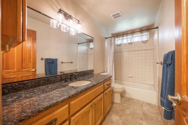 a bathroom with a granite countertop sink a toilet a mirror and shower