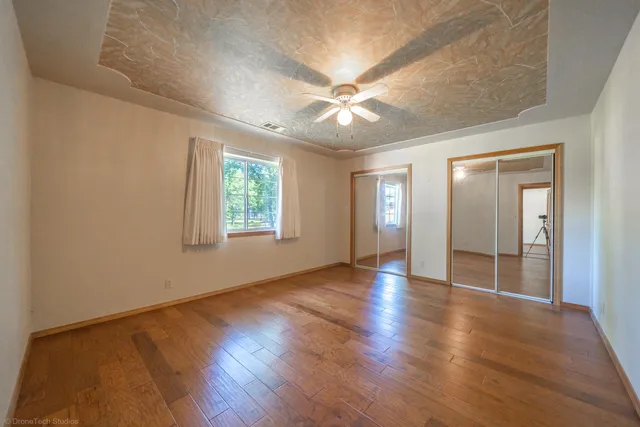 an empty room with wooden floor chandelier fan and windows