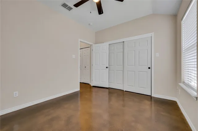 an empty room with chandelier fan and windows
