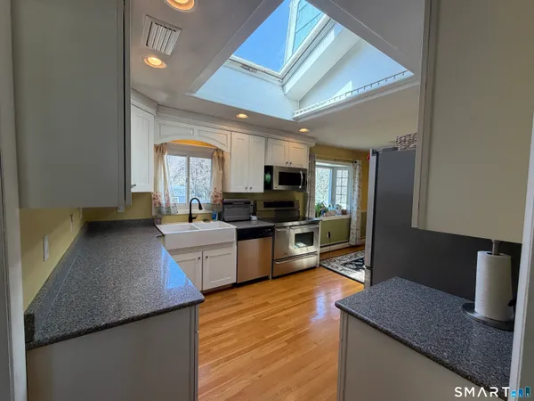 a kitchen with stainless steel appliances a stove top oven a sink a refrigerator white cabinets and wooden floor