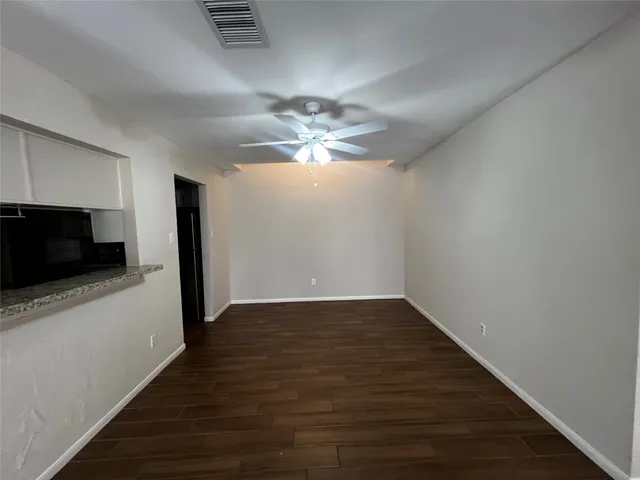 a view of an empty room with wooden floor and a ceiling fan
