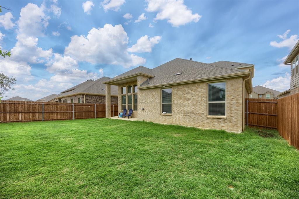 3808 High Country Road Aubrey, TX 76227 - Photo 27 of 36 Spacious backyard with a vibrant green lawn, featuring a privacy fence, a covered patio, and a brick exterior