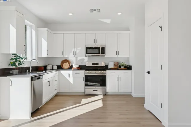 a white kitchen with stainless steel appliances granite countertop a stove a sink and a microwave