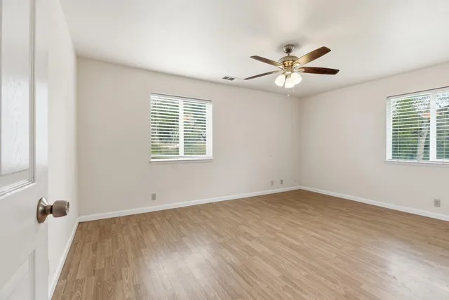 an empty room with wooden floor ceiling fan and windows