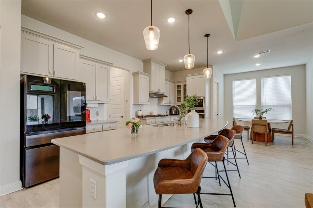 9613 Boulder Pt Road Oak Point, TX 75068 - Photo 8 of 28 Open-concept kitchen featuring an expansive island with pendant lighting, light-toned cabinetry, stainless steel appliances, and wood-finish flooring