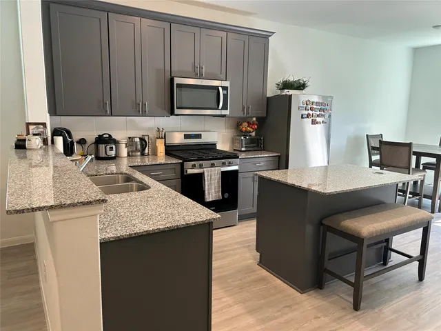 a kitchen with kitchen island granite countertop a sink dishwasher stove and microwave with wooden cabinets