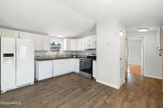 a kitchen with granite countertop a refrigerator oven a sink and white cabinets with wooden floor