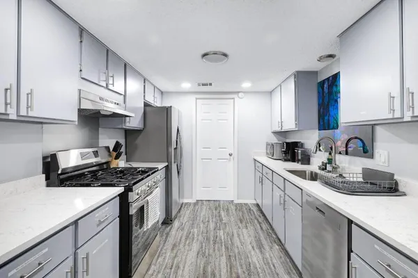 a kitchen with stainless steel appliances a sink dishwasher stove refrigerator and cabinets with wooden floor