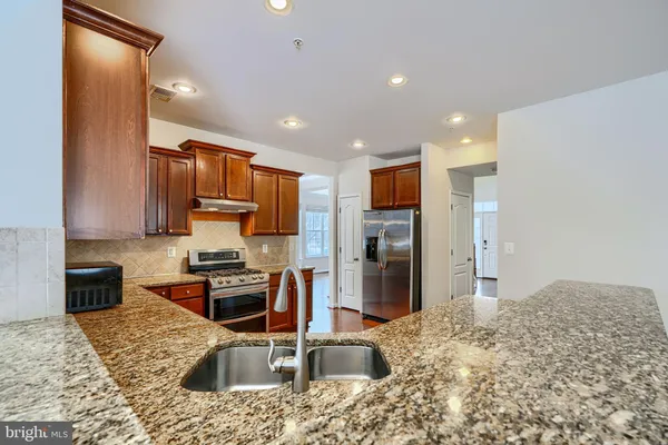 a kitchen with stainless steel appliances granite countertop wooden cabinets a sink dishwasher a stove and a refrigerator with wooden floor