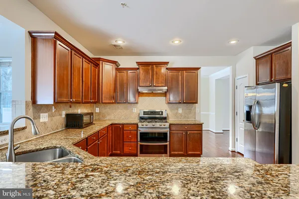 a kitchen with stainless steel appliances granite countertop a refrigerator a sink a stove and a wooden floors
