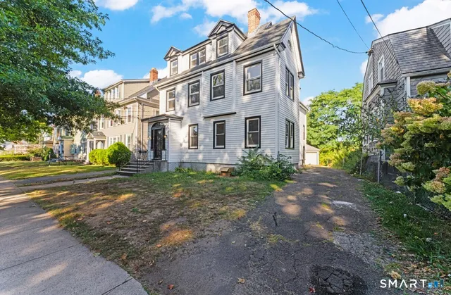 a view of a white house next to a yard with big trees