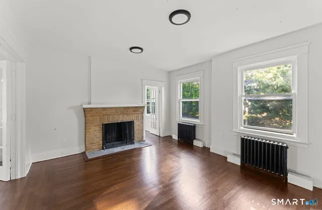 an empty room with wooden floor fireplace and windows