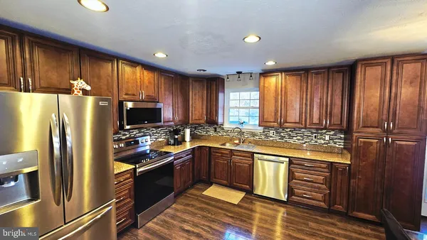 a kitchen with stainless steel appliances granite countertop a refrigerator a sink dishwasher a stove and white countertops with wooden floor