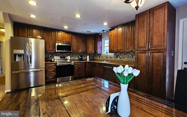 a kitchen with stainless steel appliances granite countertop a refrigerator a sink a stove a dining table and chairs with wooden floor