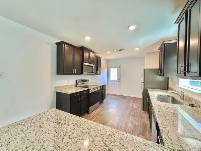 a large kitchen with stainless steel appliances kitchen island granite countertop a refrigerator stove top oven and sink