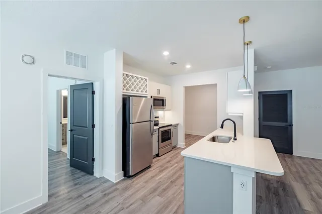 a kitchen with kitchen island a counter top space a sink a refrigerator and wooden floor