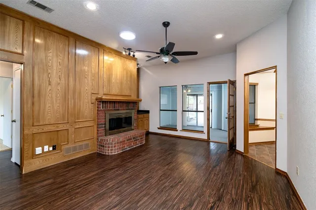 a view of an empty room with wooden floor a ceiling fan and windows