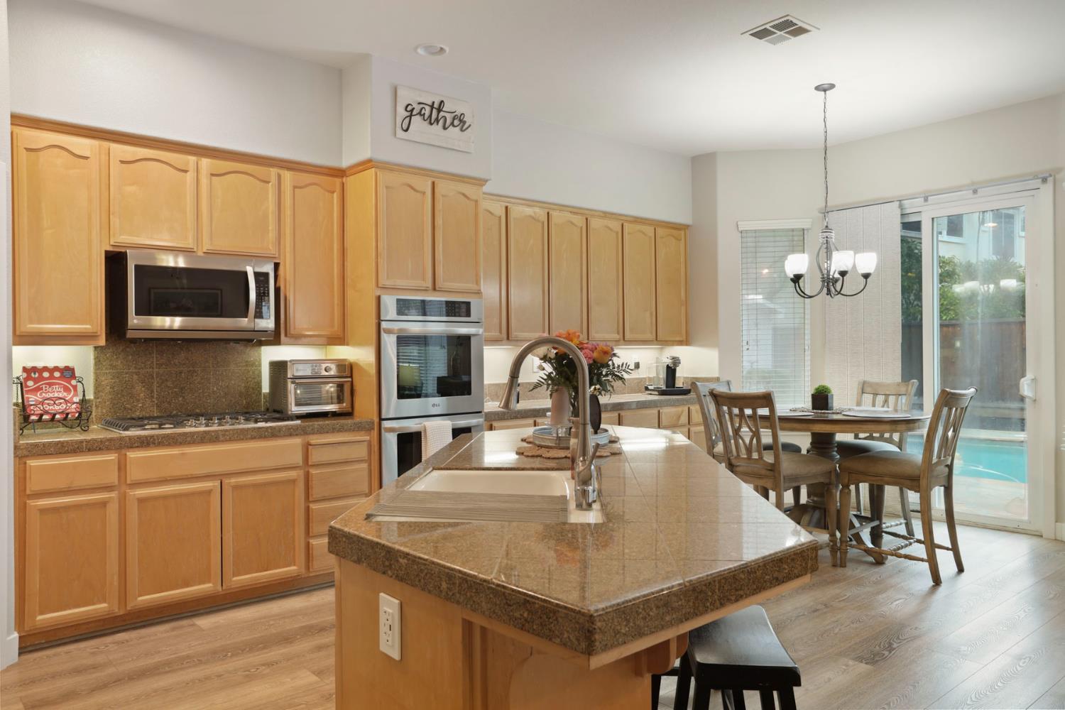 2307 Lighthouse Circle Tracy, CA 95304 - Photo 27 of 57 a kitchen with kitchen island granite countertop a stove a sink a dining table and chairs with wooden floor