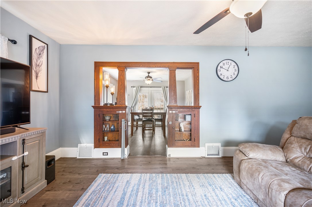 Living room with dark wood-style floors, baseboards, visible vents, and ceiling fan