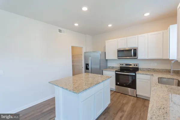 a kitchen with stainless steel appliances granite countertop a stove a sink a refrigerator and white cabinets with wooden floor