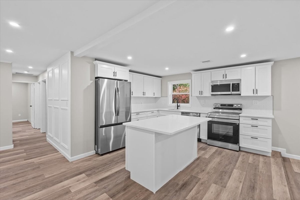 a kitchen with stainless steel appliances granite countertop a stove top oven a refrigerator and white cabinets with wooden floor