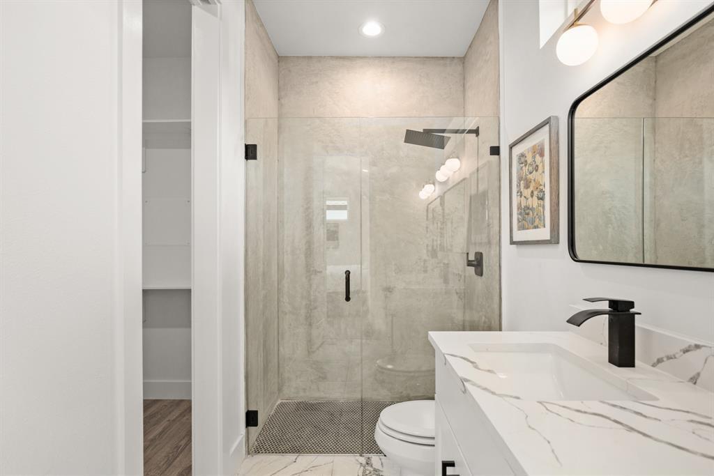 1606 Harvey Street, Unit 2 Austin, TX 78702 - Photo 14 of 22 Contemporary bathroom featuring a spacious walk-in shower with clear glass enclosure and rainfall showerhead, a white vanity with an integrated rectangular sink and veined countertop, matte black hardware, and an illuminated modern mirror
