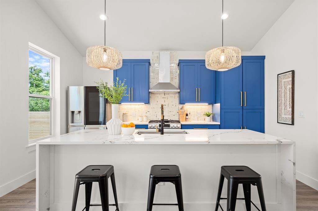 1606 Harvey Street, Unit 2 Austin, TX 78702 - Photo 3 of 22 Gourmet kitchen featuring a waterfall island with a quartz countertop, custom blue cabinetry, stainless steel appliances, and two woven pendant lights