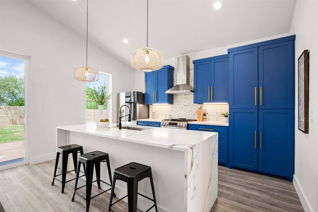 1606 Harvey Street, Unit 2 Austin, TX 78702 - Photo 5 of 22 Kitchen featuring a large waterfall island with a white countertop, blue cabinetry, stainless steel appliances, and wood-finish flooring